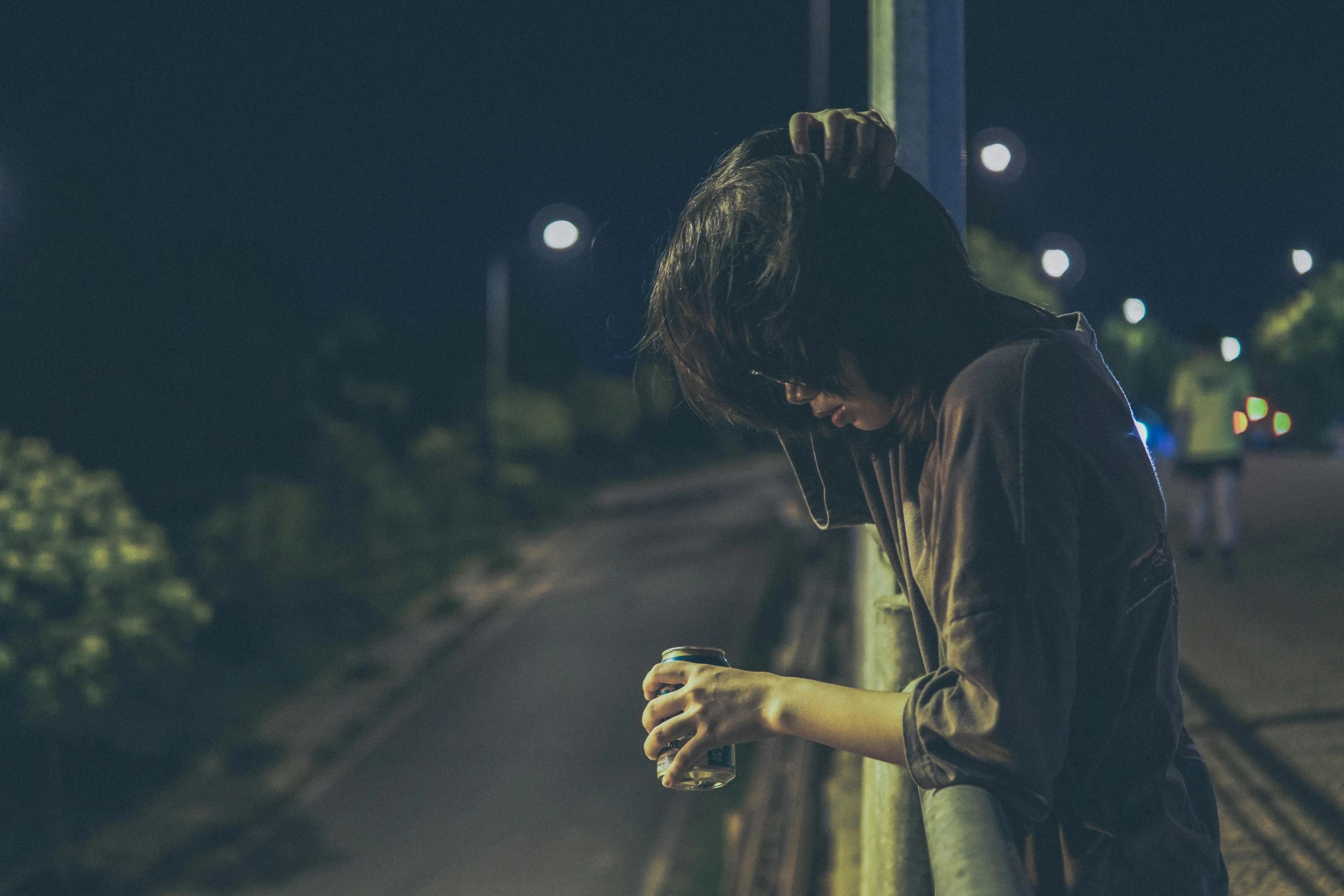 a woman looking down at her cell phone, inspired by Elsa Bleda, pexels contest winner, happening, a photo of a disheveled man, night outdoors, head bowed slightly, drinking a beer at train station