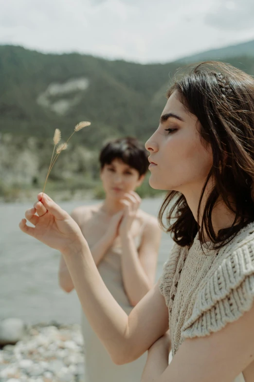 two women standing next to each other near a body of water, by Anna Boch, trending on pexels, conceptual art, holding a flower, woman with black hair, film still promotional image, twigs