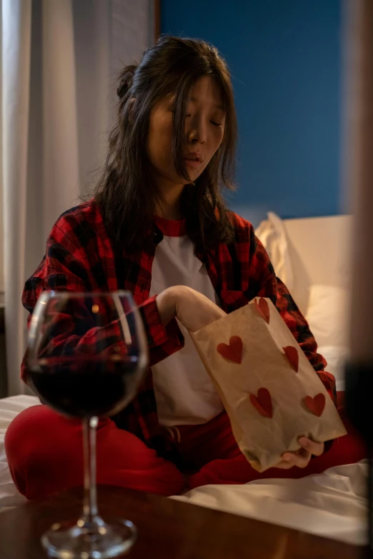 a woman sitting on a bed next to a glass of wine, dressed in red paper bags, dark vhs broken hearts, asian female, profile image