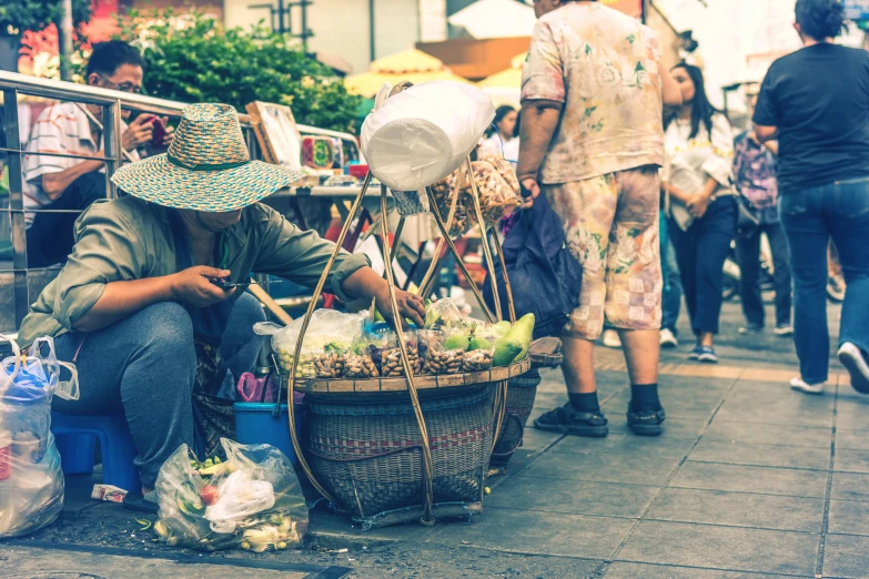 a woman sitting on the side of a street next to a basket of fruit, pexels contest winner, bangkok townsquare, avatar image, banner, pointy conical hat