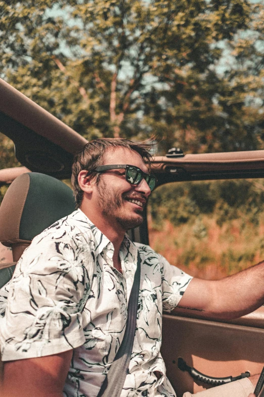 a man sitting in the driver's seat of a car, a picture, trending on unsplash, renaissance, earing a shirt laughing, patterned clothing, convertible, nature photo