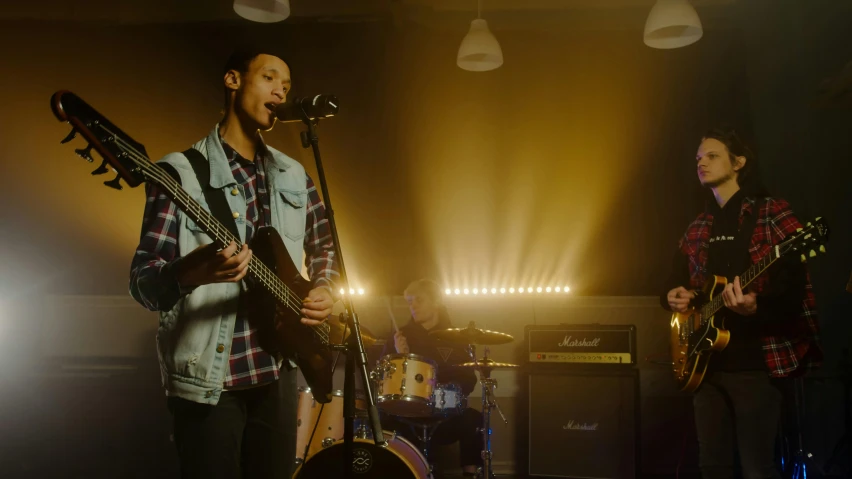 a couple of men standing next to each other on a stage, an album cover, by Jay Hambidge, pexels, performing a music video, bassist, indoor scene, teenage boy