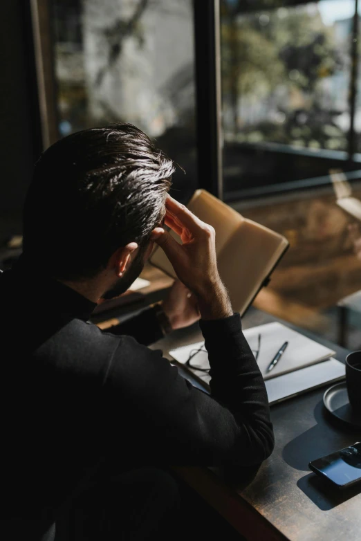 a man sitting at a table in front of a laptop, by Niko Henrichon, pexels contest winner, stressed out, holding a book, looking out of the window, gif