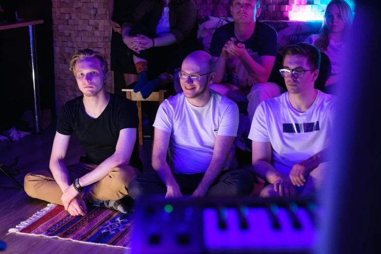 a group of men sitting on top of a wooden floor, an album cover, by Jacob Toorenvliet, unsplash, private press, lasers and neon circuits, twitch streamer / gamer ludwig, audience, looking content