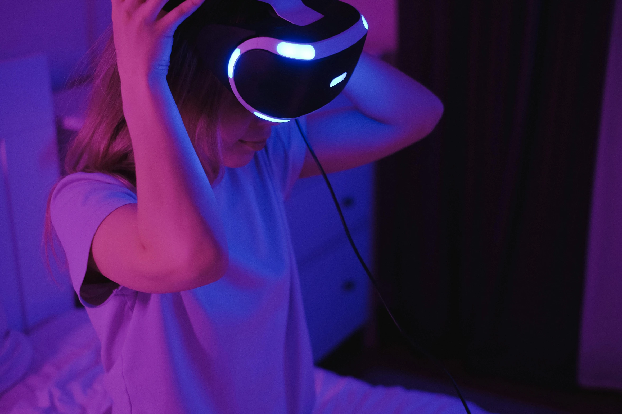 a woman sitting on a bed holding a pair of headphones, a hologram, inspired by Beeple, trending on pexels, interactive art, vr helmet, blue and purle lighting, avatar image