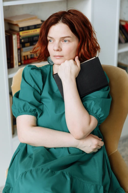 a woman sitting in a chair holding a book, dark green dress, with red hair, in a dark teal polo shirt, jovana rikalo