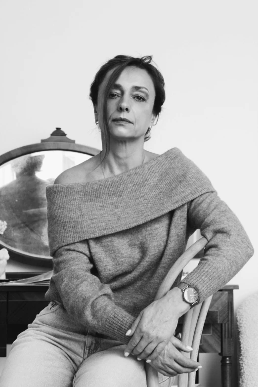 a black and white photo of a woman sitting on a chair, inspired by Caterina Tarabotti, antipodeans, arm around her neck, 5 5 yo, standing elegantly, looking serious