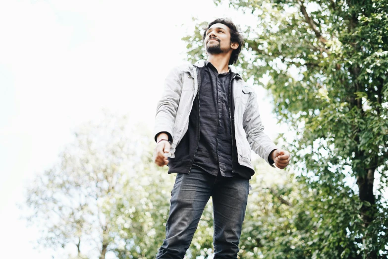 a man standing on a skateboard in a park, inspired by Thota Vaikuntham, happening, press shot, looking upward, a man wearing a black jacket, expressing joy