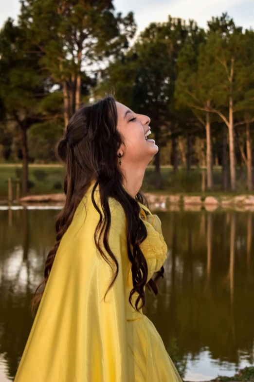 a woman in a yellow raincoat standing in front of a lake, mutahar laughing, smiling as a queen of fairies, profile image, floating robes