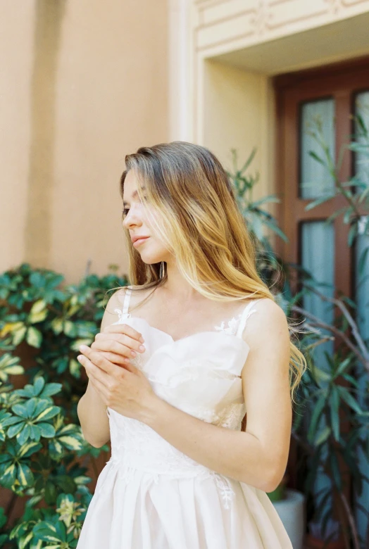 a woman in a white dress standing in front of a building, by Sara Saftleven, unsplash, renaissance, medium format. soft light, bride, wearing a camisole, solemn gesture