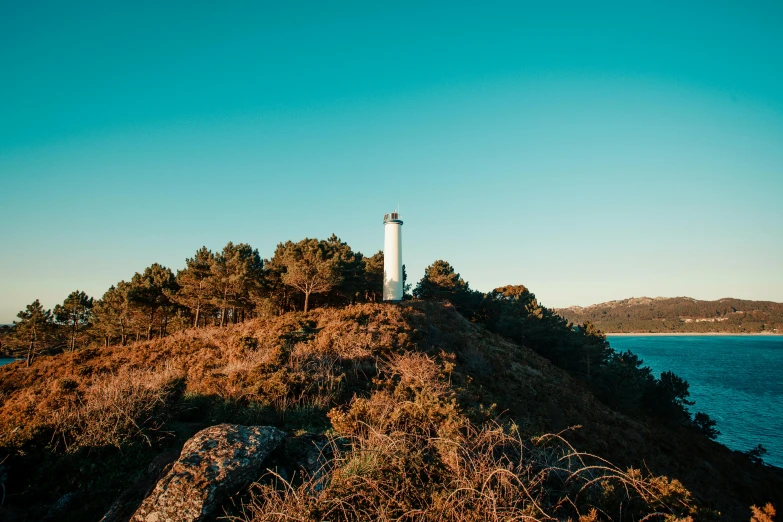 a lighthouse sitting on top of a hill next to the ocean, arrendajo in avila pinewood, lachlan bailey, lightbox, crisp photo