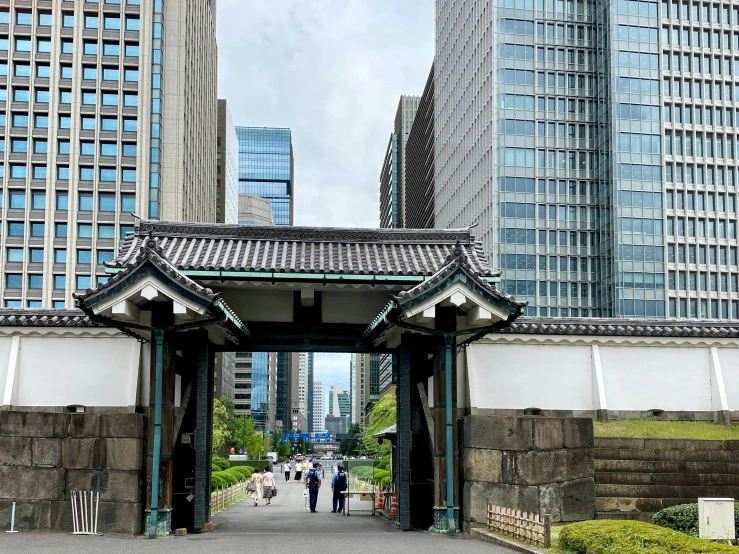 a gate in the middle of a city with tall buildings in the background, sōsaku hanga, skyscrapers with greenery, people walking around, tradition, instagram post