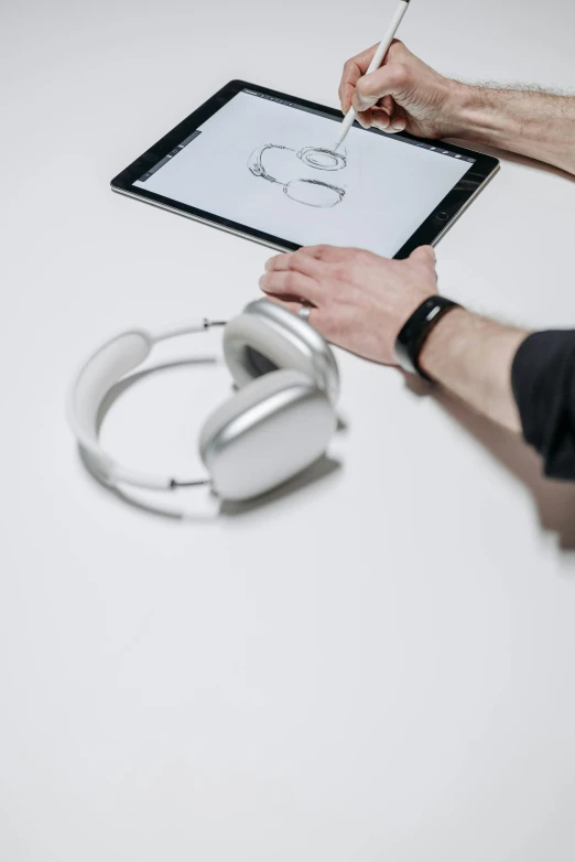 a man sitting at a table with a tablet and headphones, a digital rendering, unsplash, bauhaus, white and silver, classic product design, sitting with wrists together, detail shot