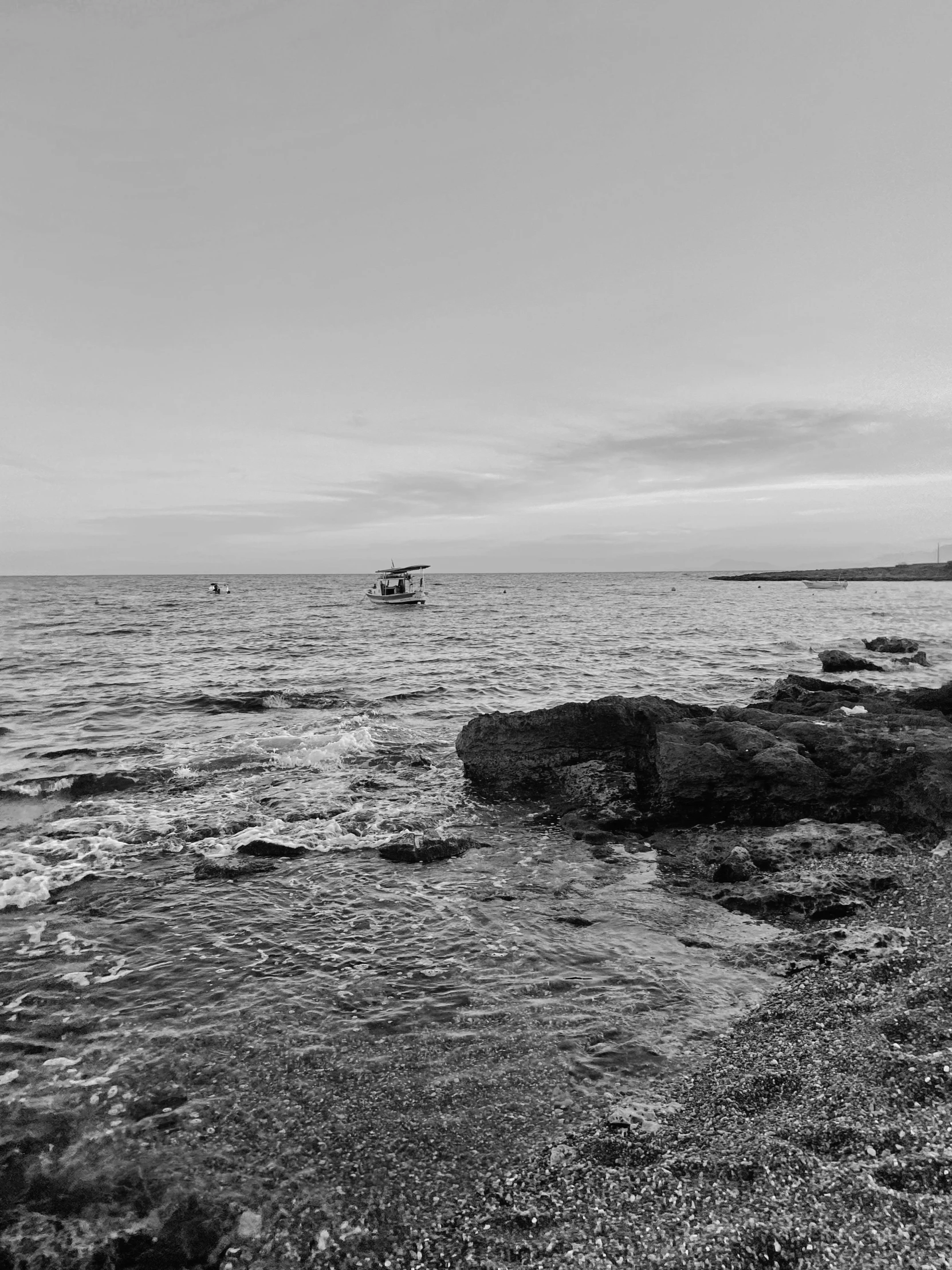 a black and white photo of the ocean, by Alexis Grimou, small boat in the foreground, fineartamerica, rocky beach, today\'s featured photograph 4k