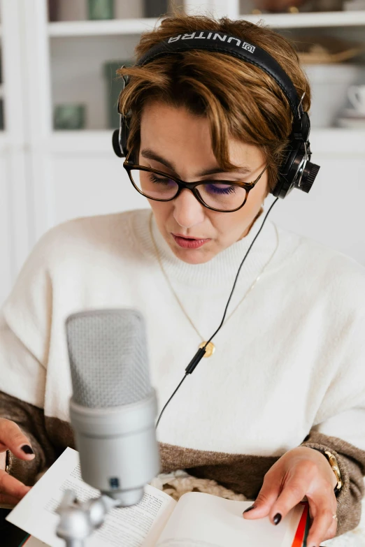 a woman reading a book while wearing headphones, a cartoon, trending on pexels, sitting in front of a microphone, wearing a turtleneck and jacket, studio qualit, wearing square glasses