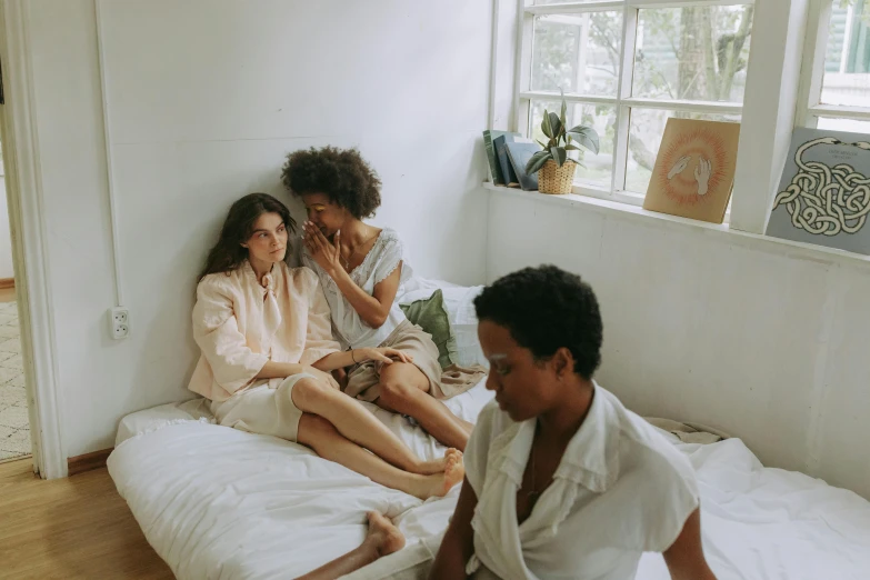 a couple of people sitting on top of a bed, trending on pexels, three women, muted palette mostly white, with brown skin, hila klein