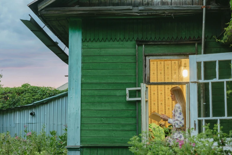 a woman looking out the window of a green house, inspired by Isaac Levitan, pexels contest winner, summer evening, exterior, cardboard, panoramic shot