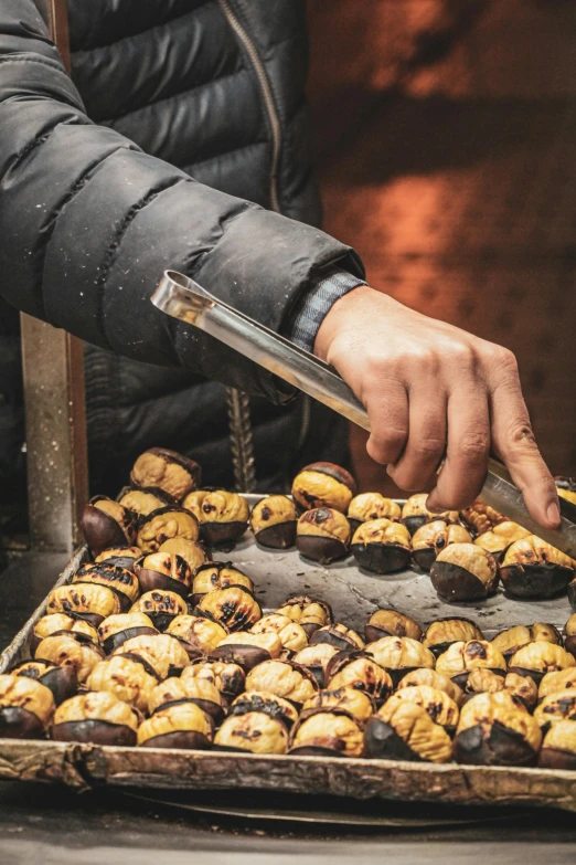 a person holding a knife over a tray of pastries, hurufiyya, licorice allsort filling, street market, snails, warm