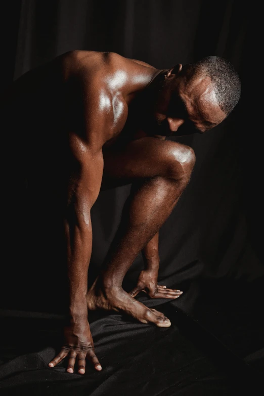 a man squatting in front of a black background, inspired by Robert Mapplethorpe, hyperrealism, brown skin like soil, bare foot, his palms are sweaty, instagram photo