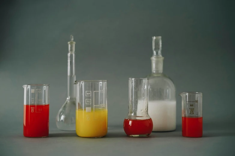 a group of glass beakers filled with liquid, a still life, unsplash, scarlet and yellow scheme, on grey background, formulae, from left