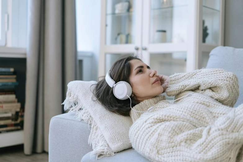 a woman laying on a couch with headphones on, trending on pexels, wearing a white sweater, pokimane, winter season, easygoing