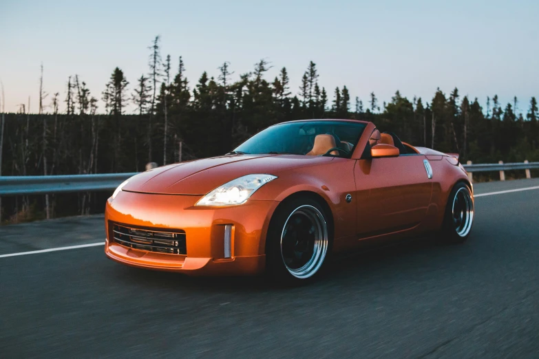 an orange sports car driving down a road, unsplash, aftermarket parts, soft top, tokyo drift, front lit