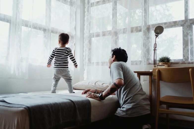 a man standing next to a little boy on a bed, pexels contest winner, looking out window, kids playing, walking down, full daylight