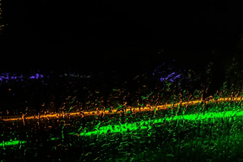 a blurry photo of a street at night, an album cover, inspired by Bruce Munro, unsplash, lyrical abstraction, bright green dark orange, driving rain, gold green blue purple, vivid green lasers