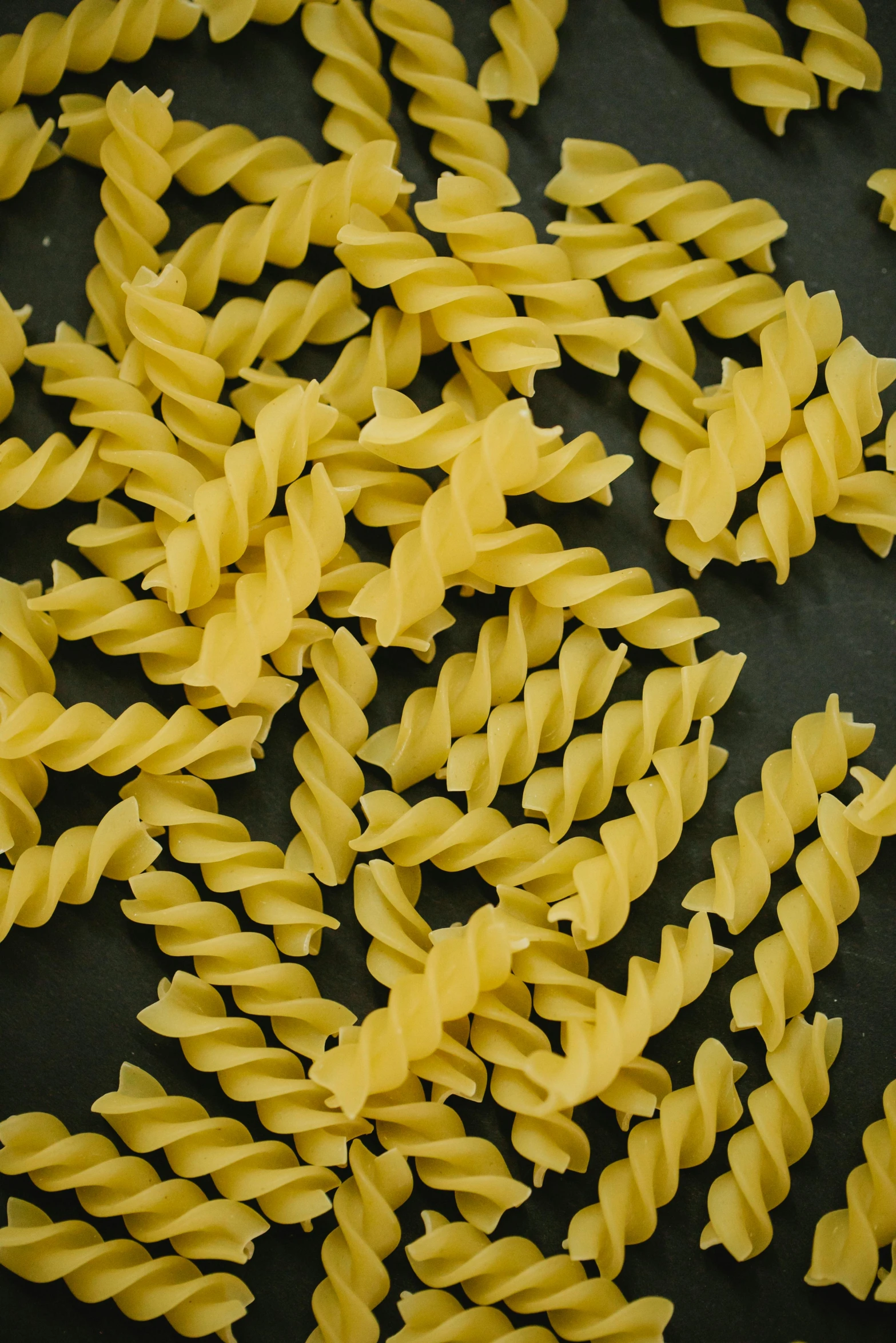 a pile of pasta sitting on top of a black surface, spirals, 4l, patterned, yellow