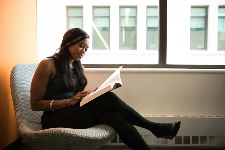 a woman sitting in a chair reading a book, by Carey Morris, pexels contest winner, dark skinned, sat in an office, profile image, casually dressed