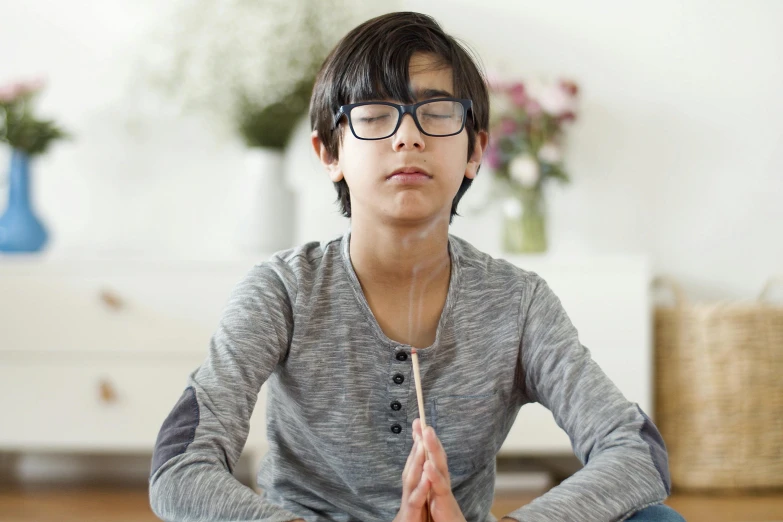 a little boy sitting in the middle of a yoga pose, an album cover, trending on pexels, hurufiyya, with glasses, praying posture, teen boy, neuroscience