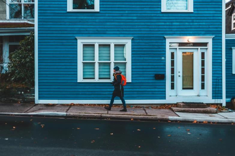 a person standing in front of a blue house, by Julia Pishtar, pexels contest winner, walking to work, quebec, the man have a backpack, neighborhood themed