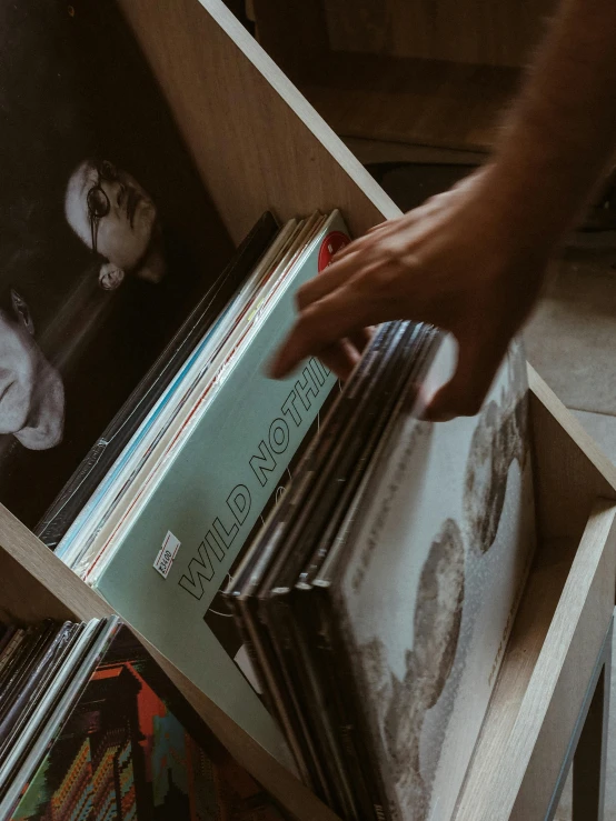 a person reaching for a record in a wooden box, an album cover, pexels contest winner, analytical art, book shelves, low quality photo, thumbnail