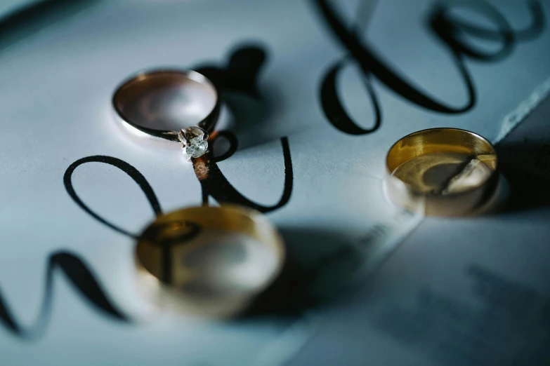 a couple of wedding rings sitting on top of a piece of paper, by Sylvia Wishart, pexels contest winner, letters, bangles, zoomed in shots, 15081959 21121991 01012000 4k