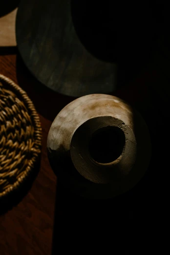 a wicker basket sitting on top of a wooden table, a still life, inspired by George Ault, trending on unsplash, japanese vase, underexposed lighting, circle forms, an unknown ethnographic object
