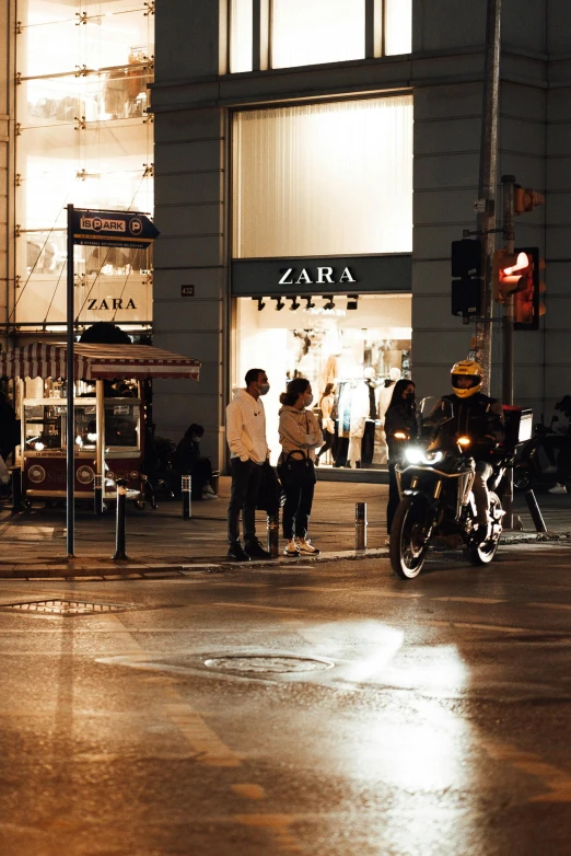 a man riding a motorcycle down a street next to a tall building, people shopping, zaba style, during the night, vienna city