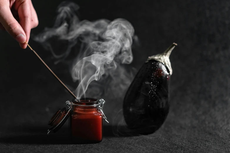 a person lighting a candle next to an eggplant, by Emma Andijewska, pexels contest winner, auto-destructive art, red smoke, holding hot sauce, miniature photography closeup, grey