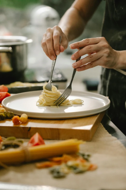 a person in a kitchen preparing food on a plate, served with pasta, gourmet and crafts, using fork, superior