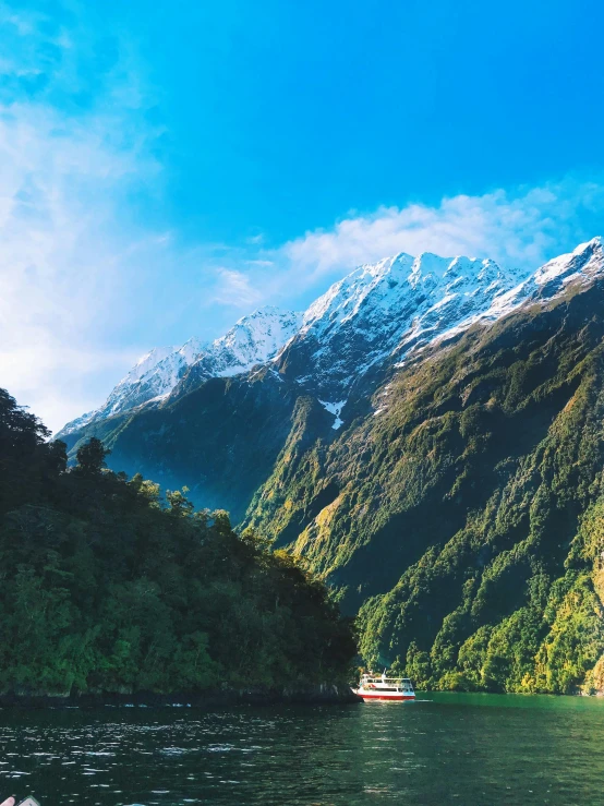 a boat on a body of water with mountains in the background, new zeeland, majestic snowy mountains, towering high up over your view, today\'s featured photograph 4k