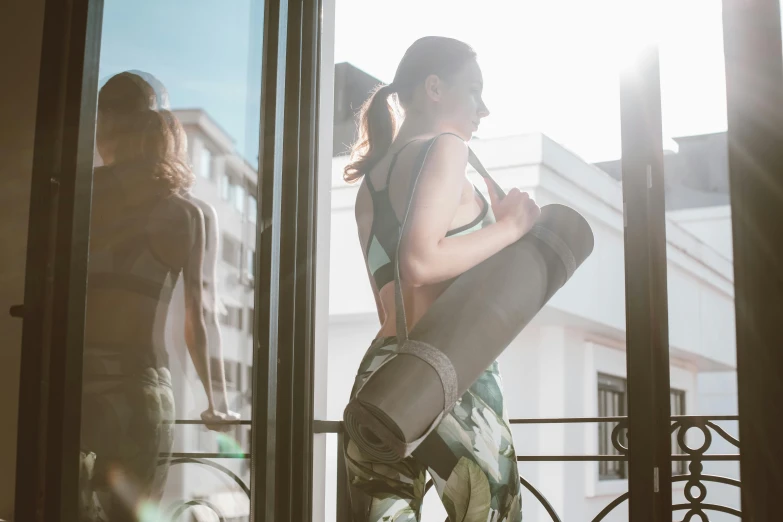 a woman standing in front of a window holding a snowboard, arabesque, wearing fitness gear, afternoon sunshine, woman holding another woman, thighs focus