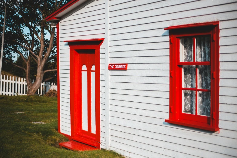 a white house with a red door and window, an album cover, by Peter Churcher, pexels contest winner, new zealand, cottage close up, museum photograph, bright signage