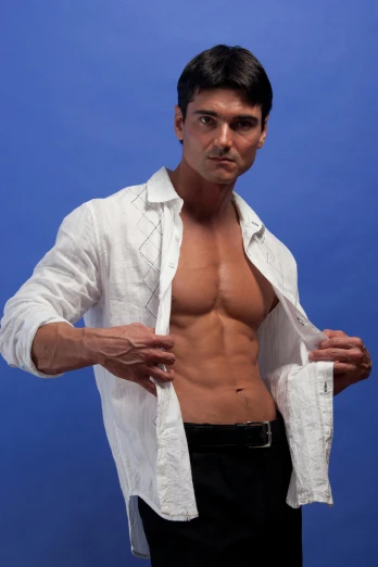 a shirtless man standing in front of a blue background, an album cover, by Juan Carlos Stekelman, wearing a white button up shirt, [ rigidly defined abs ]!!, taken in the late 2010s, fashion model pose