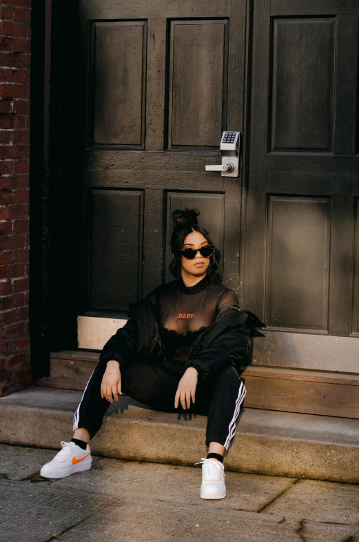 a woman sitting on a step in front of a door, inspired by Ion Andreescu, trending on pexels, trending on r/streetwear, woman with black hair, shades, black body