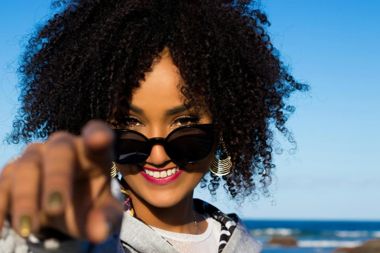 a close up of a person holding a camera, pexels contest winner, afrofuturism, smiling fashion model, with sunglass, wave a hand at the camera, natural hair