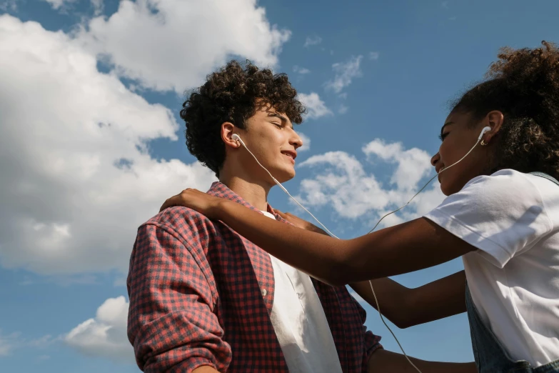 a couple of young people standing next to each other, trending on pexels, fantastic realism, black teenage boy, skies behind, earbuds, loving embrace