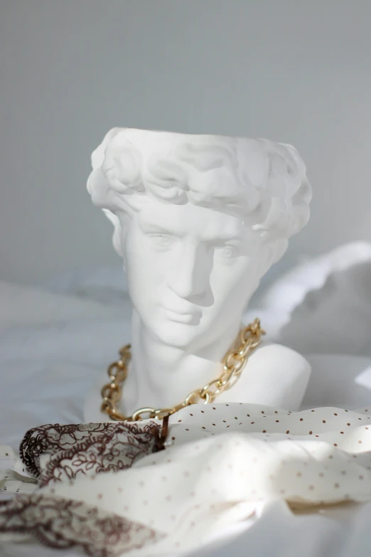 a statue sitting on top of a bed covered in white sheets, a marble sculpture, inspired by Antonio Canova, trending on pexels, wearing a bandana and chain, white vase, gold detailed collar, teenager