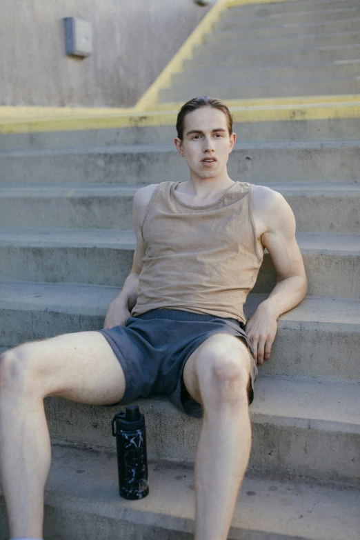 a man sitting on some steps with a bottle of beer, inspired by Jean Malouel, reddit, wearing a tank top and shorts, nonbinary model, wearing leotard, lachlan bailey