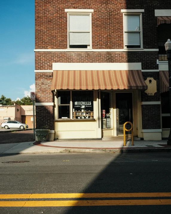 a tall brick building sitting on the side of a road, storefront, photo in style of tyler mitchell, yellow awning, michael okuda