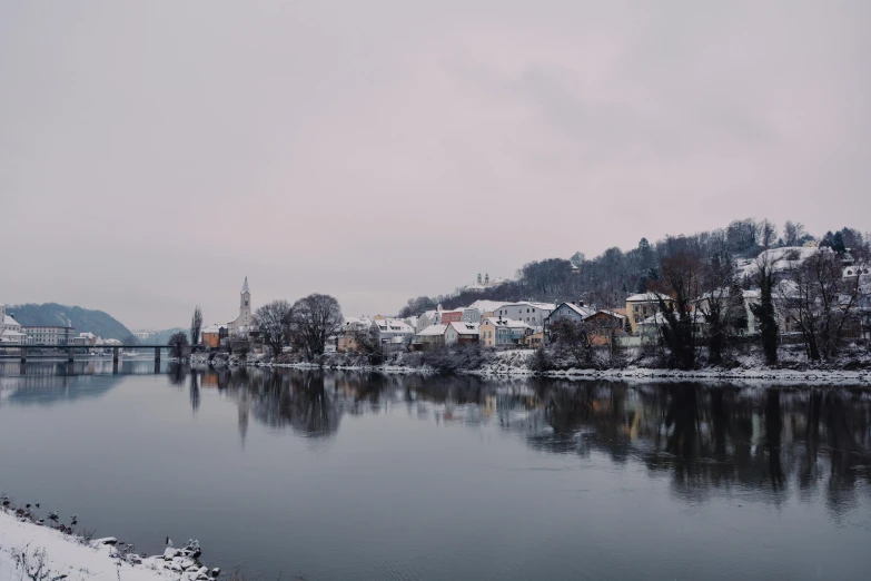 a body of water surrounded by snow covered trees, by Adam Szentpétery, pexels contest winner, romanticism, town in the background, gray sky, austro - hungarian, detailed medium format photo