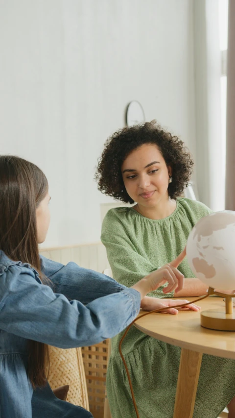 two women sitting at a table looking at a globe, trending on pexels, low quality photo, balloon, varying ethnicities, teenage girl